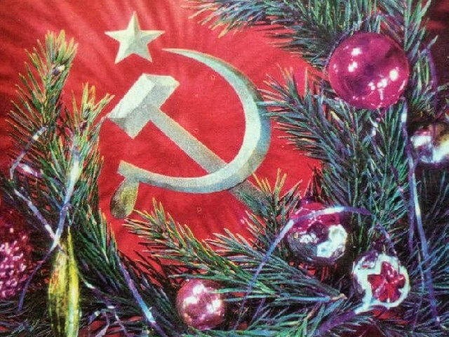 A golden hammer and sickle on a red backdrop framed by a foreground of spruce branches decorated with glass ornaments and tinsel